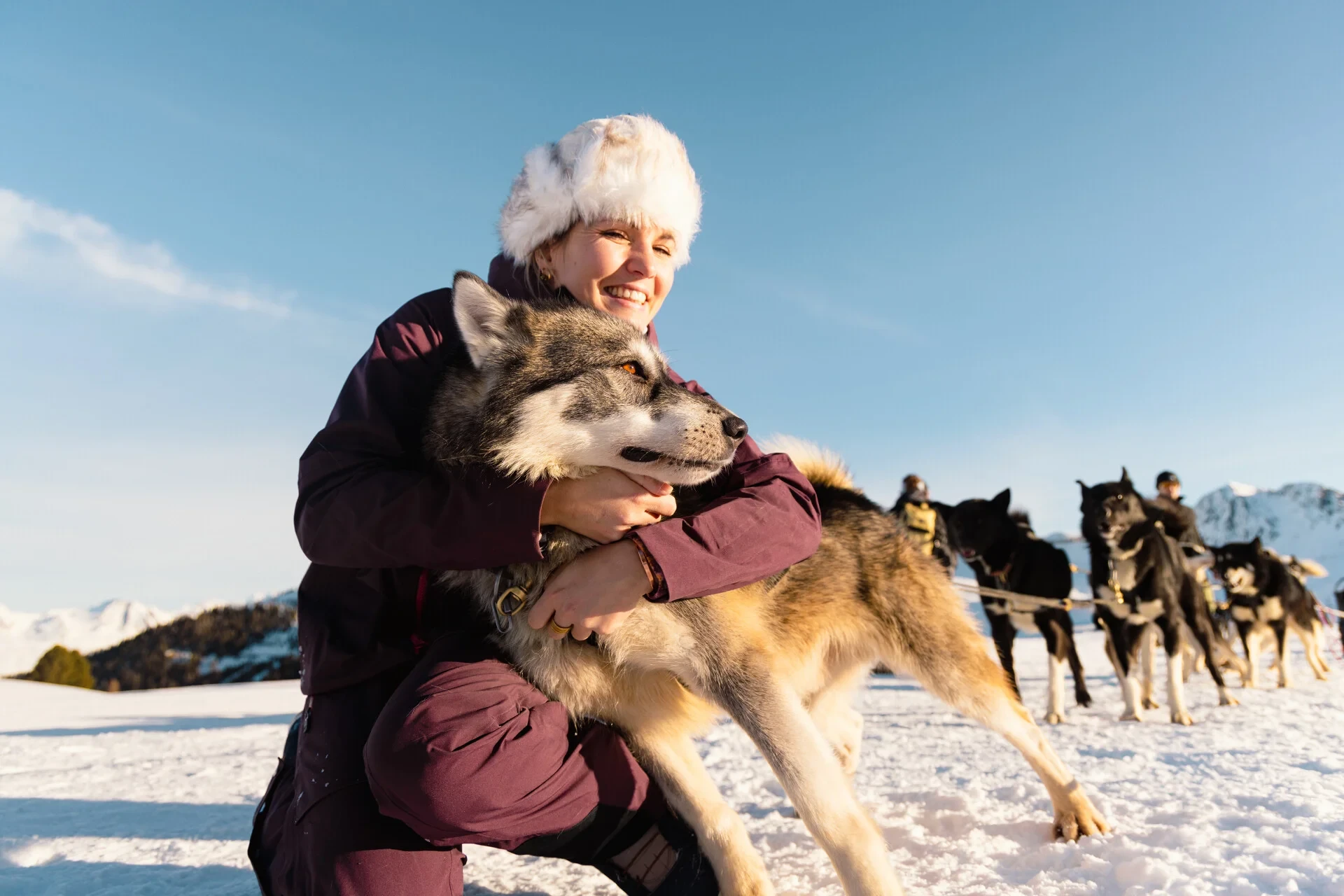 Femme câlinant un chien de traîneau dans la neige.