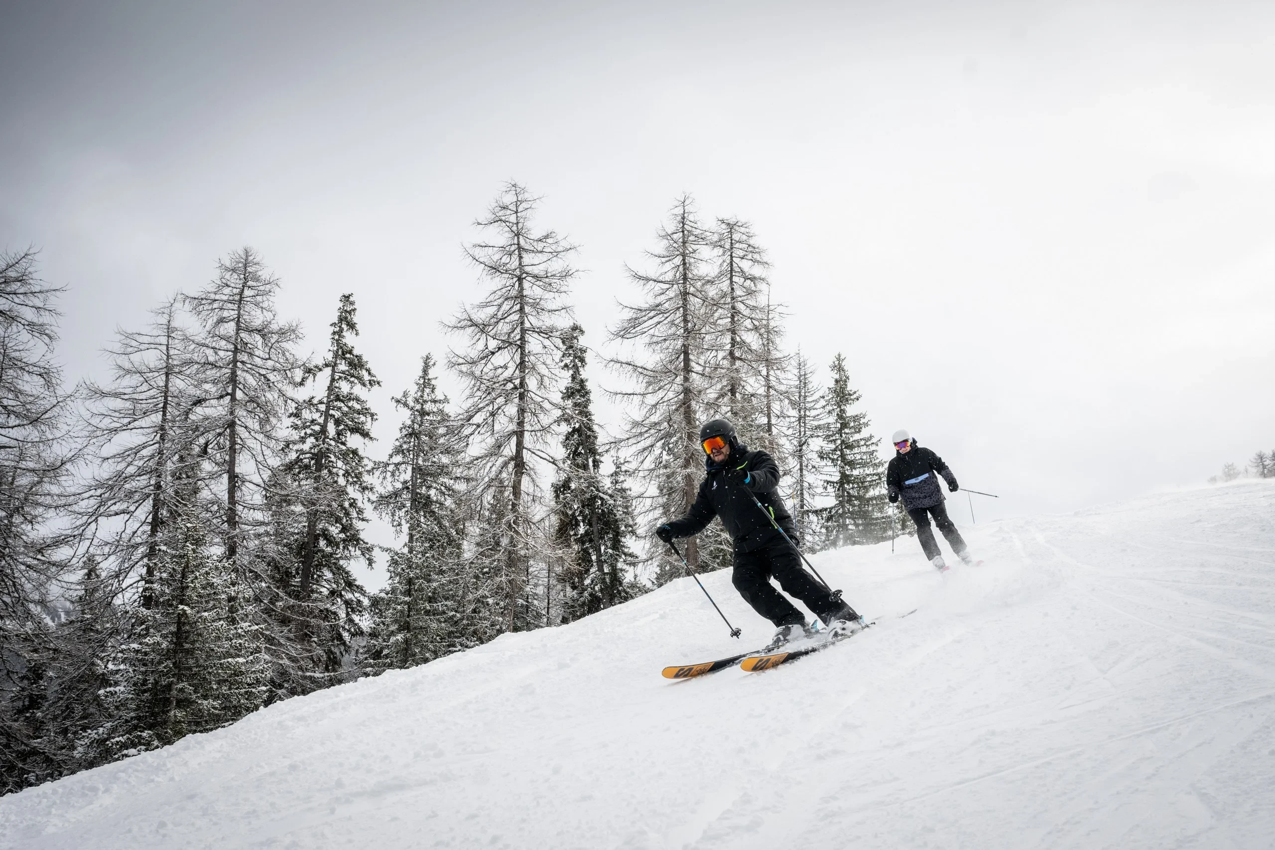 Deux skieurs sur une piste enneigée en forêt.