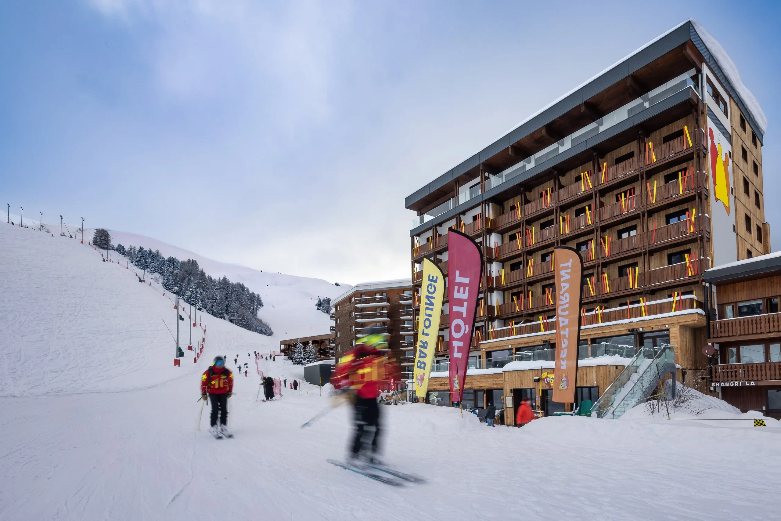 Skieurs devant hôtel en station de ski enneigée.