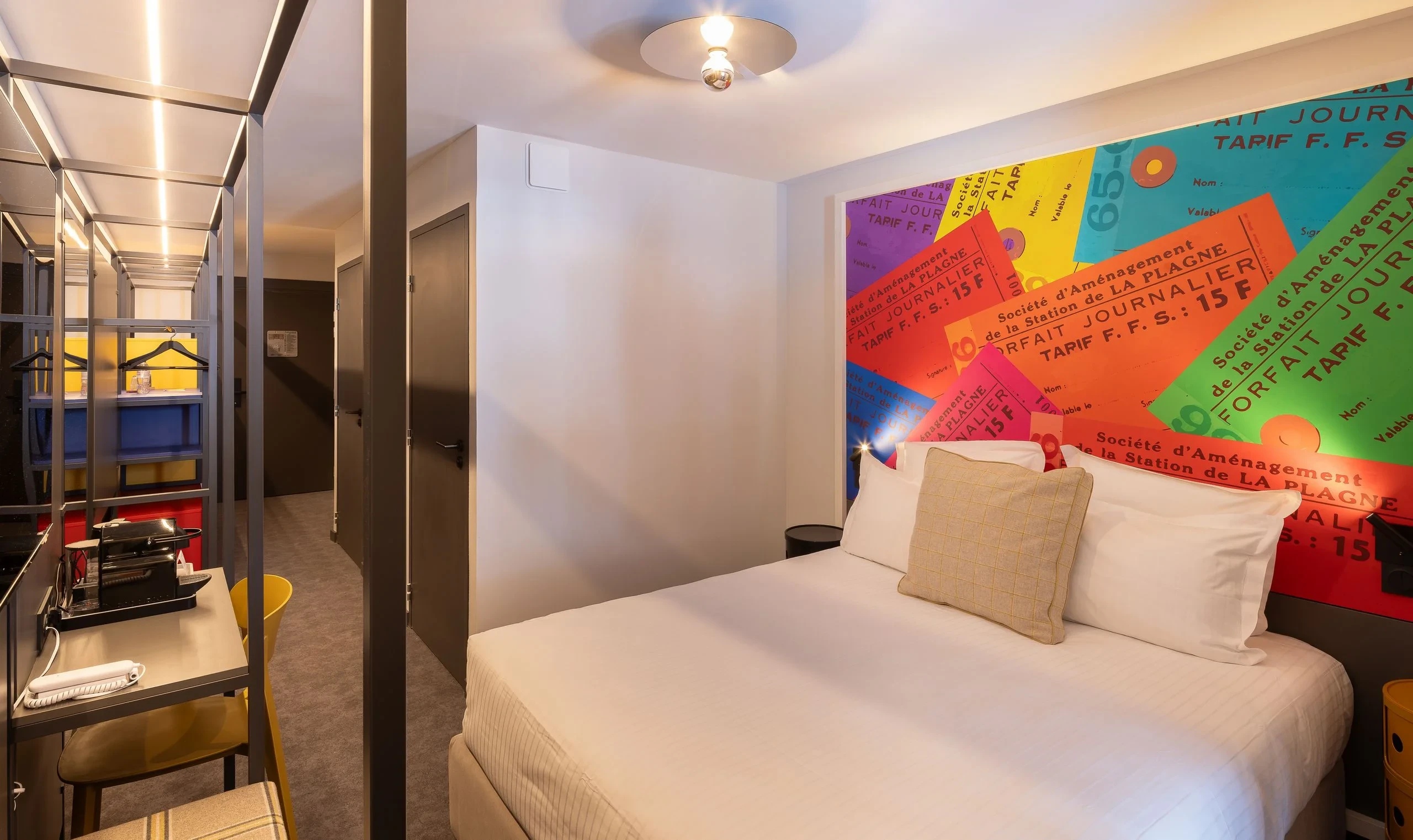Chambre d'hôtel colorée avec lit double et bureau.