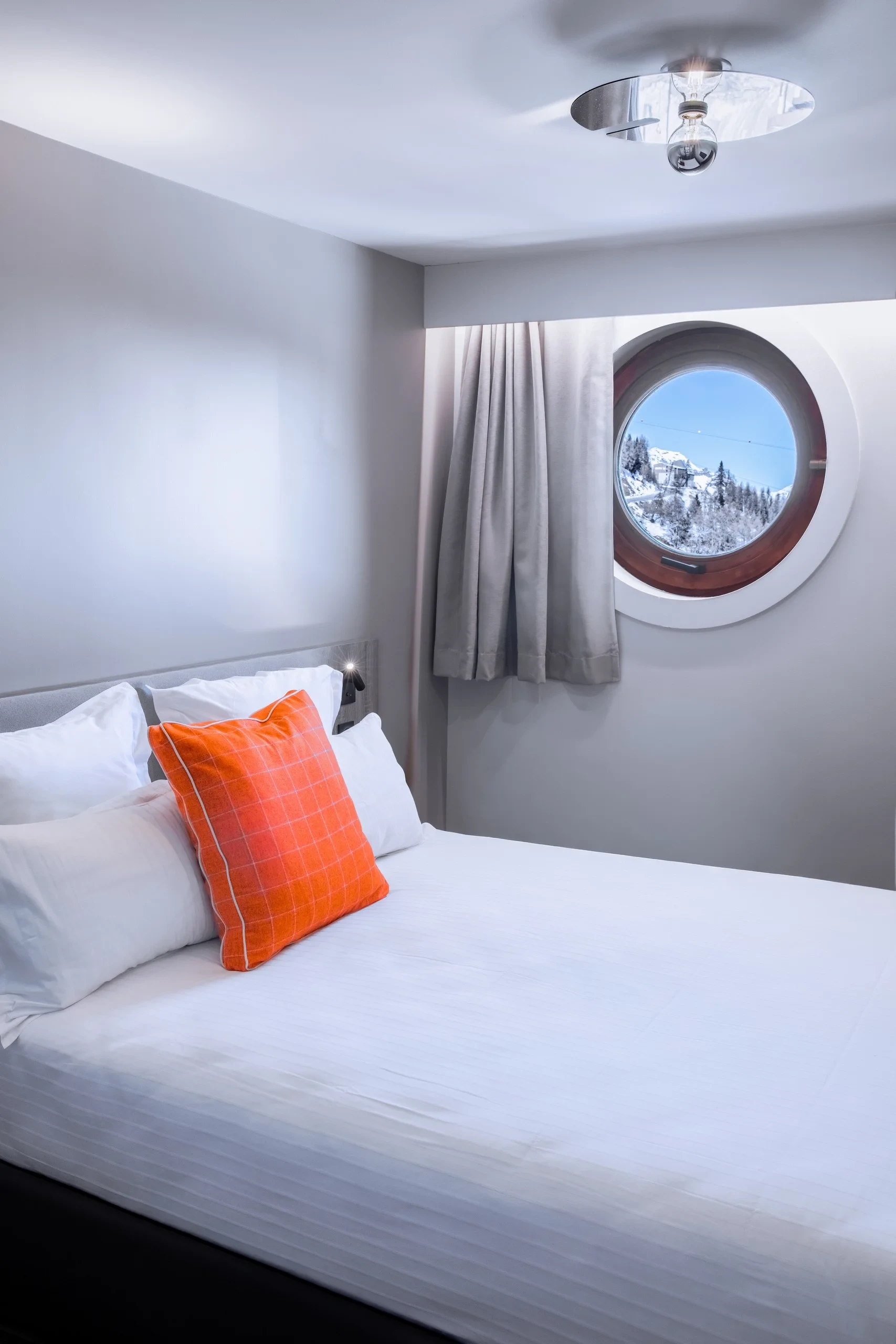 Chambre avec hublot et coussin orange.