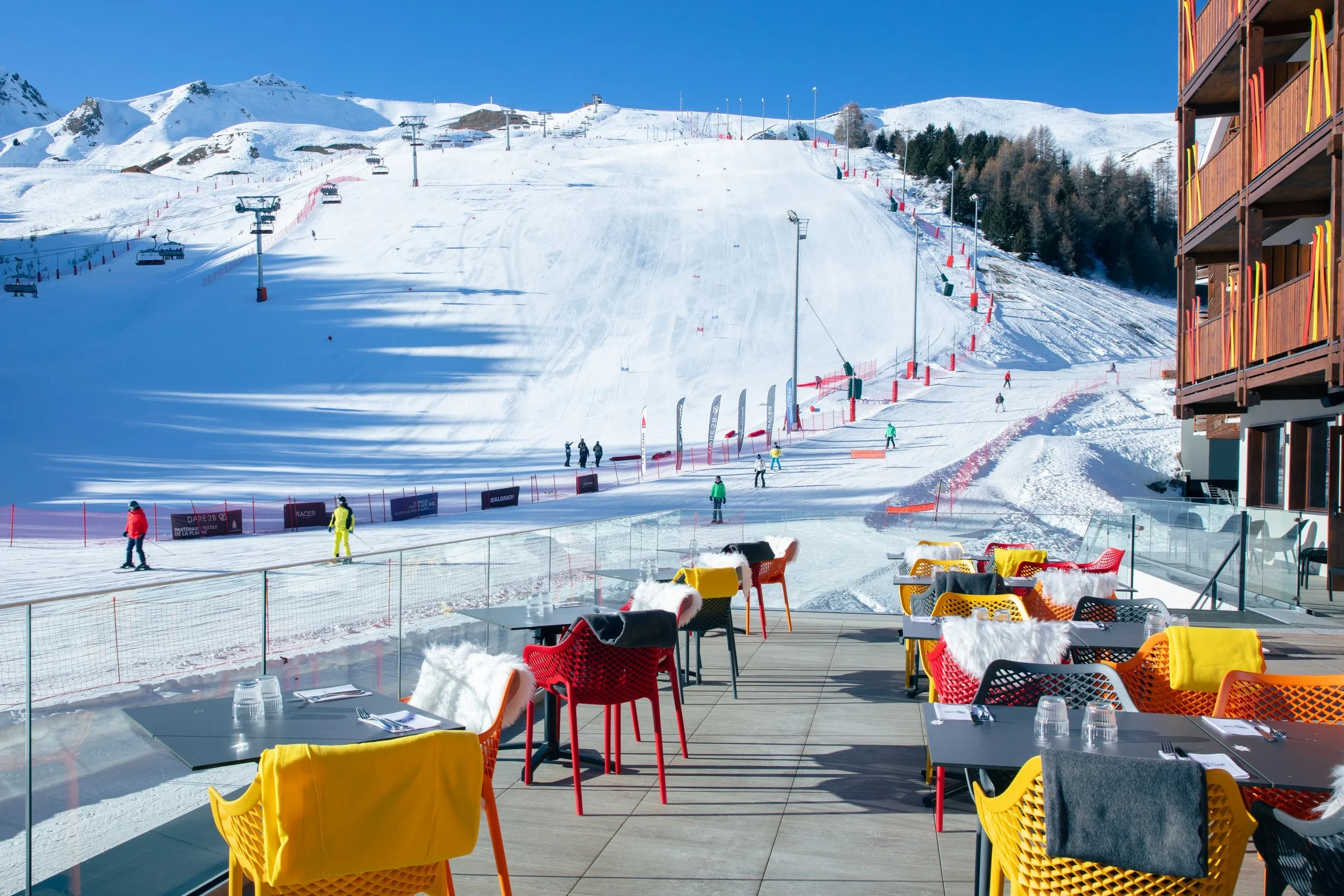 Terrasse ensoleillée avec vue sur piste enneigée.