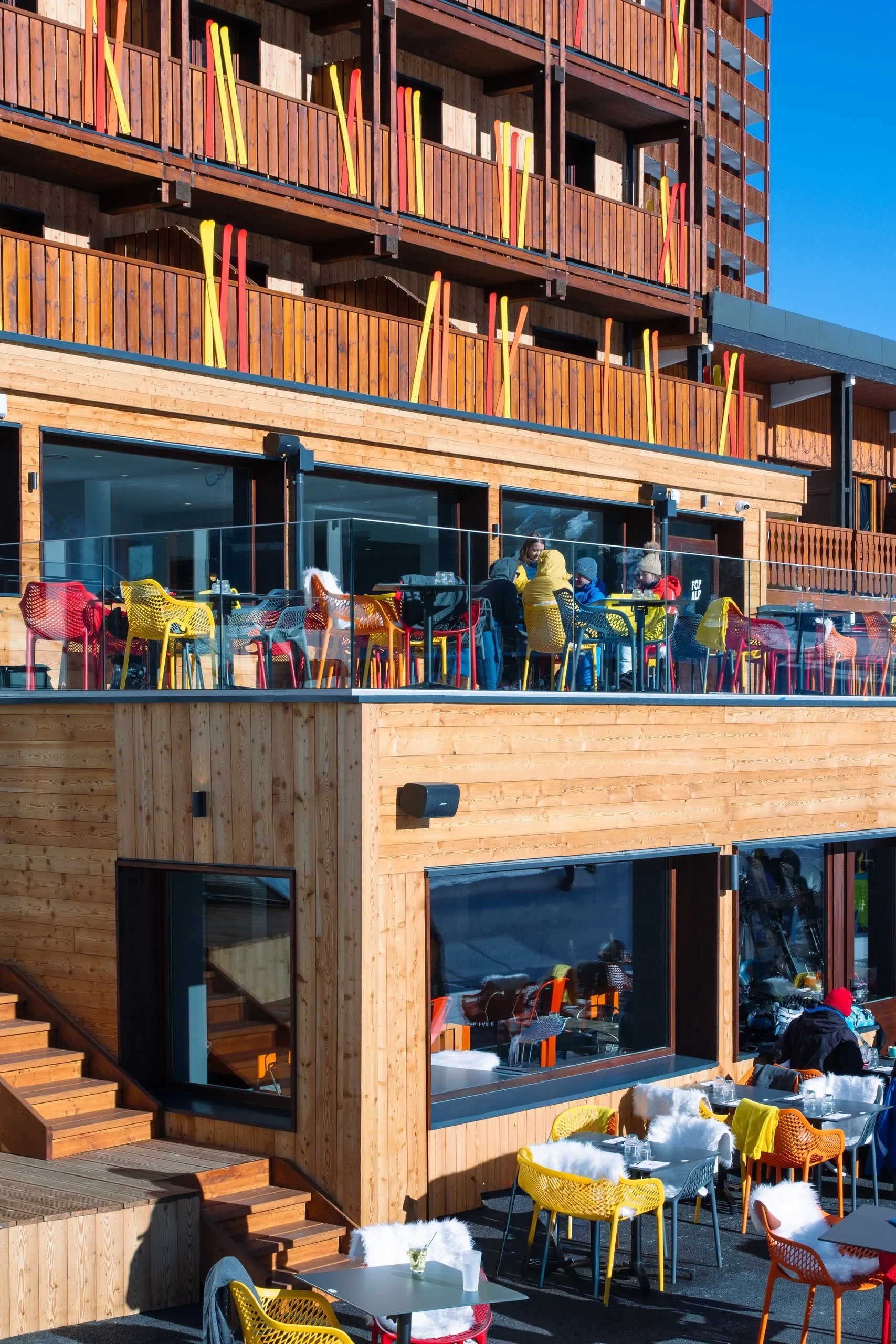 Terrasse colorée avec chaises et tables, bâtiment en bois.