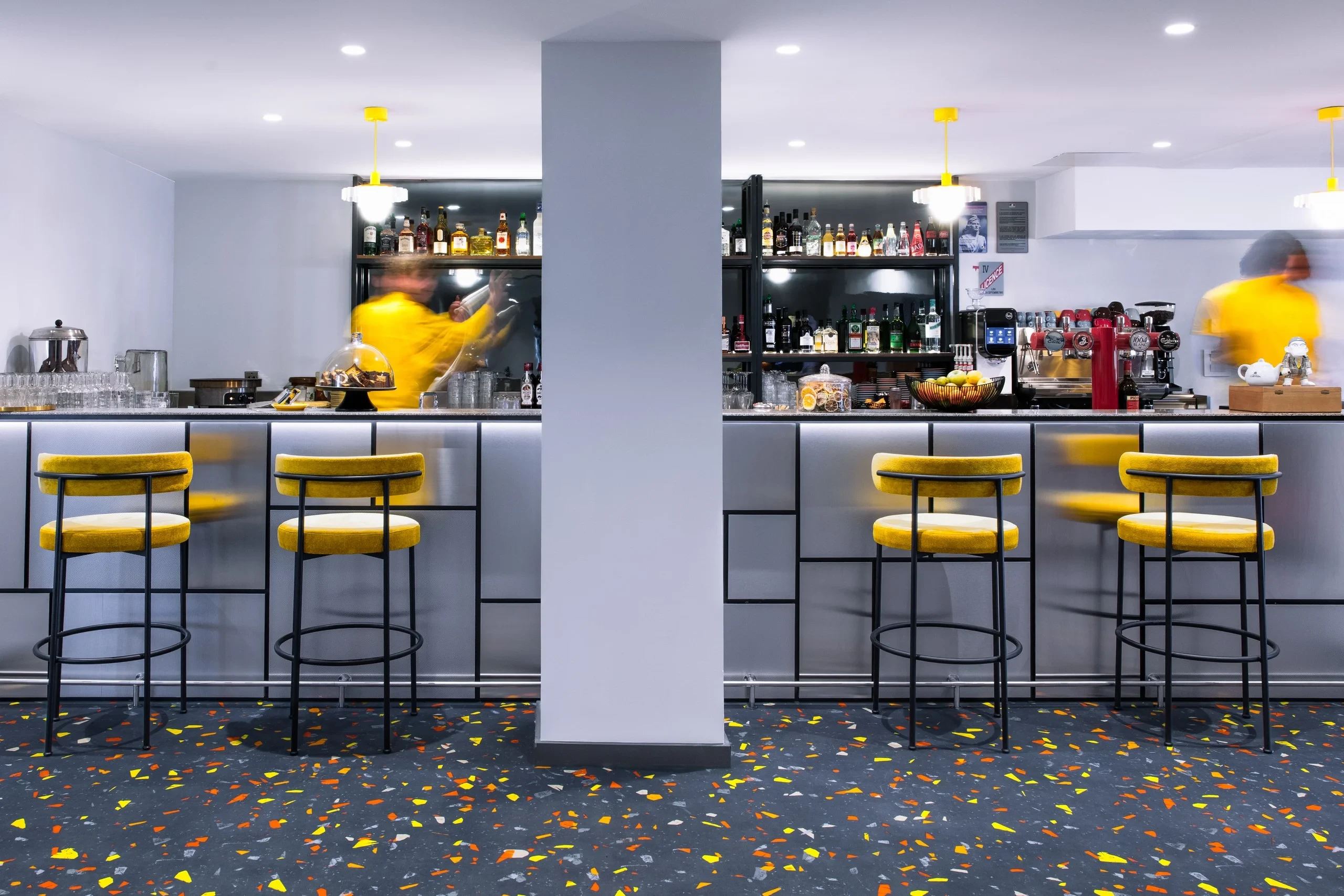 Bar moderne avec tabourets jaunes et sol coloré.