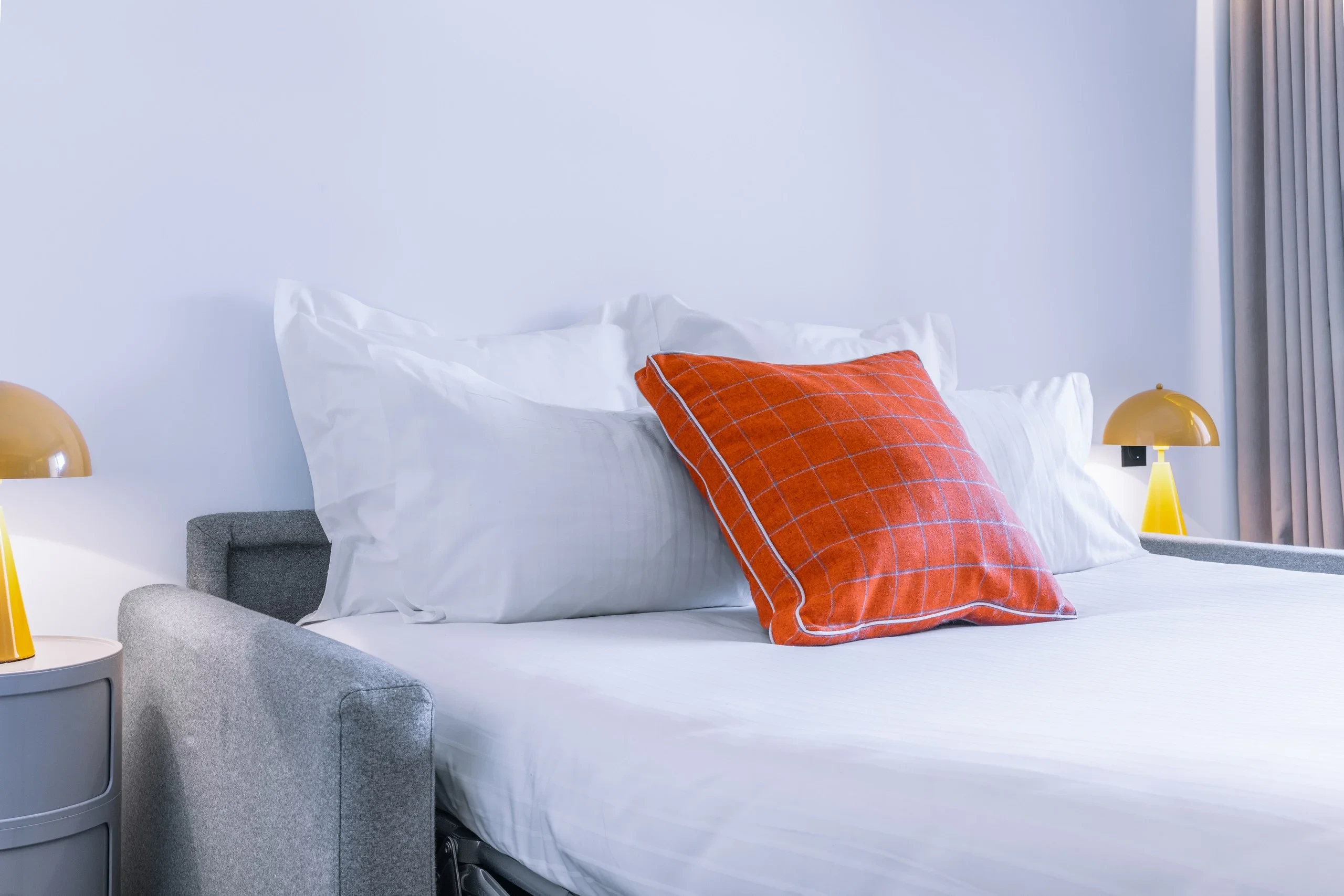 Lit avec coussin rouge sur draps blancs.